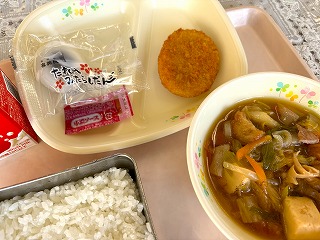 ピンクのトレーに給食が左から時計回りに牛乳、お月見だんご、さつまいもコロッケ（パックソース）、すきやき煮、ごはんと並んでいる写真