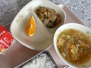 ピンクのトレーに給食が左から時計回りに牛乳、オレンジ、中華丼の具、春雨スープ、ごはんと並んでいる写真