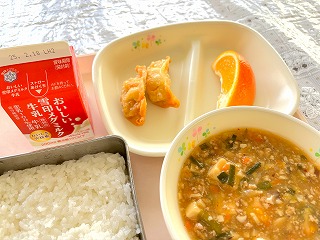 ピンクのトレーに給食が左から時計回りに牛乳、揚げぎょうざ、いよかん、マーボー豆腐、ごはんが並んでいる写真