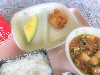 ピンクのトレーに給食が左から時計回りに牛乳、メロン、揚げぎょうざ、マーボー豆腐、ごはんと並んでいる写真