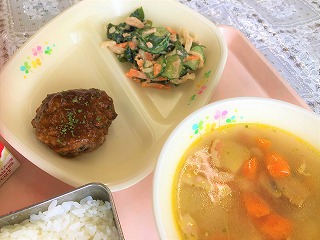 ピンクのトレーに給食が左から時計回りに牛乳、手作りハンバーグ、わかめと大根のサラダ、コンソメスープ、ごはんが並んでいる写真