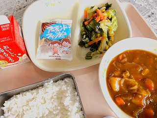 ピンクのトレーに給食が左から時計回りに牛乳、アーモンドフィッシュ、海藻サラダ、ポークカレー、ごはんが並んでいる写真