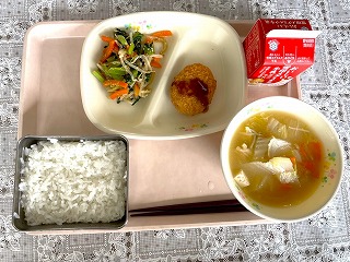 ピンクのトレーに給食が左から時計回りに小松菜のごまあえ、かつおカツ（パックソース）、牛乳、白菜と油あげのみそ汁、ごはんが並んでいる写真