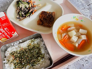 ピンクのトレーに給食が左から時計回りに牛乳、ふか肉の竜田揚げ、ひじきサラダ、さつま汁、ふりかけがかかったごはんが並んでいる写真