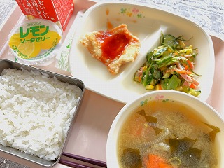 ピンクのトレーに給食が左から時計回りに牛乳、レモンソーダゼリー、チキン南蛮、りっちゃんサラダ、わかめ汁、ごはんが並んでいる写真