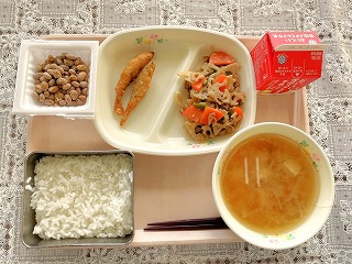 ピンクのトレーに給食が左から時計回りに納豆、わかさぎ天ぷら、れんこんきんぴら、牛乳、油あげともやしのみそ汁、ごはんが並んでいる写真