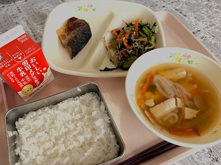 ピンクのトレーに給食が左から時計回りに牛乳、さばのスタミナ焼き、小松菜ののりあえ、お雑煮、ごはんが並んでいる写真