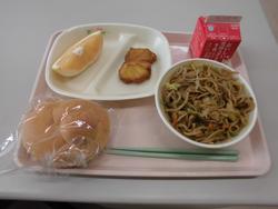 ピンクのトレイにパン、チキンナゲット、やきそば、グレープフルーツ、牛乳が並んだ給食の写真