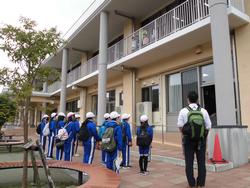 青いジャージに白い帽子をかぶった中学生が2階建ての校舎の前に並んで立っている写真