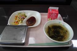 ピンクのトレイにご飯、ハンバーグトマトソース、キャベツとコーンのソテー、わかめのスープ、牛乳が並んだ給食の写真