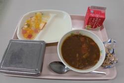 ピンクのトレイにご飯、夏野菜カレー、牛乳、フルーツのゼリー和え、アーモンドフィッシュが並んだ給食の写真