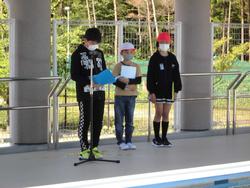 マイクスタンドの前に立ち、原稿を読んでいる子どもと、その横に立っている2人の子どもの様子を捉えた写真