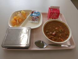 ピンクのトレイにご飯、チキンカレー、フルーツのゼリーあえ、アーモンドフィッシュ、牛乳が並んだ給食の写真