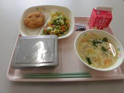 ピンクのトレイにご飯、手作りポテトコロッケ、キャベツとベーコンのソテー、たまごとチンゲン菜のスープ、牛乳が並んだ給食の写真