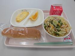 ピンクのトレイにパン、ツナオムレツ（ケチャップ）、アスパラガスとベーコンのスパゲティー、オレンジ、牛乳が並んだ給食の写真