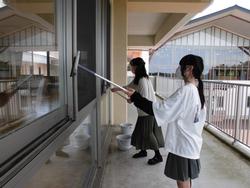窓拭き用具を持った2人の女子生徒が、校舎のベランダで窓の清掃している様子の写真