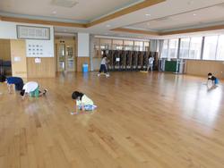 広い木目調の床の部屋で、数人の子どもたちがぞうきんやモップを使って床掃除をしている様子の写真