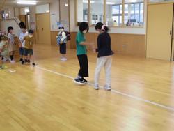 二人の女子児童が木製の床に引かれた白い線上で、じゃんけんを行っている様子の写真