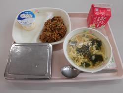 ピンクのトレイの上に、ごはん、夏野菜のドライカレー、わかめと卵のスープ、フローズンヨーグルト、牛乳パックが並べられた給食の写真