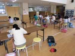 玄関ホールに複数の長机が並べられ、座った子供たちがそれぞれプリント学習や読書など、静かに課題に取り組んでいる様子の写真