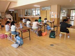 玄関ホールで、複数の子供たちが机に向かって熱心に勉強や読書などに取り組んでいる様子を後方から写した写真