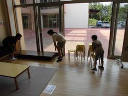 玄関ホールのガラス戸の前で、複数の児童がテーブルや椅子などの片づけをしている様子の写真