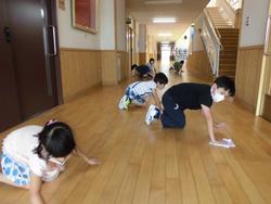 校内の長い廊下で複数の子どもたちが雑巾を手に床を四つん這いで拭き掃除をしている、清掃活動の様子の写真