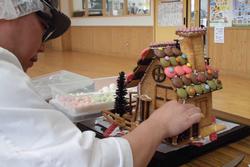 カラフルなマカロンなどのお菓子で屋根を飾った家を丁寧に仕上げているお菓子職人の写真