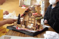 子どもと一緒に完成間近のお菓子の家を見ながら話しているお菓子職人の写真