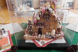 正面に丸い窓や雪の飾りがある家をケースに入れて展示しているお菓子の家の写真