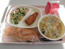 ピンクのトレイに、ブロッコリーのサラダ、南三陸産たらフライ、ワンタンスープ、パン、牛乳パックが載っている給食の写真