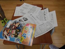 生徒の机の上に、「かんぺき！総しあげ」と書かれた冊子と複数のプリントが乱雑に置かれている様子を真上から撮影した写真