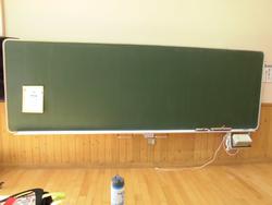 左側に1枚の紙が貼られている、何も文字が書かれていない、きれいに掃除がされた黒板を写した写真