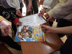 「かんぺき！総しあげ」と書かれた冊子とプリントが置かれた机を囲んで8人の生徒たちが机の上に手を差し出し、親指と人差し指を交差させてハートを作っている写真