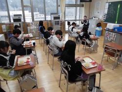 教室の中で児童が机に給食を並べて食べている写真