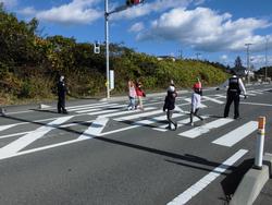 信号機のある横断歩道を右手を上げ児童が渡っている様子を警察官が指導している交通安全教室の写真