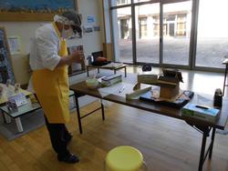 帽子に黄色のエプロンを着た人が机の上で作業の準備をしているお菓子の家作りの写真