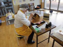 小さな椅子に座って家型の土台に装飾をしているお菓子職人の写真