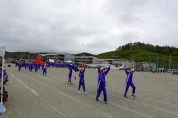 前の4人が旗を持って行進し、その後ろに赤組の旗を持った生徒を先頭に子供達が行進する様子の写真