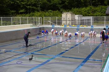 学校のプールの中に、たくさんの5･6年生が入って先生がブラシで掃除をしている様子の写真