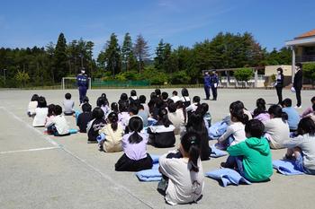 運動場で南三陸消防署の方が話するのを子供達が体育座りをして聞いている写真