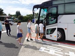 左手には引率者と思われる大人が見守っているなか、数人の子供たちがバスの乗車口に列をなし、次々に乗り込んでいく様子の写真