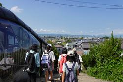 引率の先生やキャップを被りリュックを背負った子供たちが、街を見下ろす傾斜のある階段を下りている様子の写真