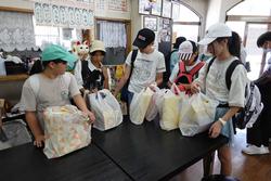 飲食店の様な店内で、キャップを被りリュックを背負った子供たちがお土産の入った袋をテーブルに並べている様子の写真