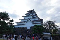 少し曇り気味の空の下、石垣の上に建っている城郭建築を模した白壁の鶴ヶ城を写した写真