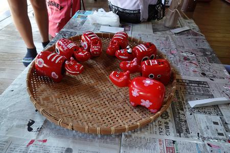 新聞紙が敷かれた台の上にざるが置かれ、ざるに桜の花柄などが描かれた赤く色づけされた7つの牛の形をした赤べこが乾燥されている写真