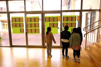 4人の子供たちが校舎の廊下の大きな窓ガラスに貼り付けられた書きぞめをじっと見ている写真