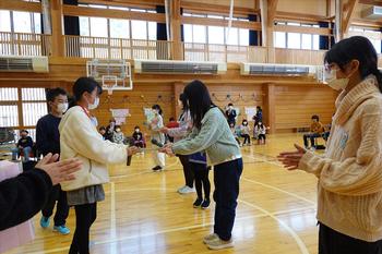 周りで他の児童たちが見ているなか、左側に立つ女の子がプレゼントを6年生に手渡している場面の写真