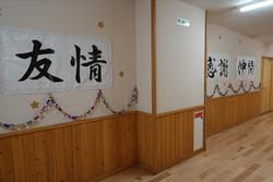 金色の星や輪飾りが飾り付けられている木目調の壁と白い壁で構成された廊下の壁に、「友情」「感謝」「仲間」などの文字が書かれた横断幕が飾られている写真