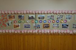 木の板と白い壁でできた廊下に、ピンクの花飾りで装飾された中に6年間の思い出の写真が壁に展示されている写真